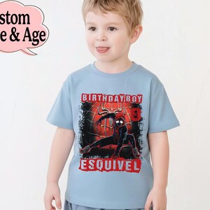 Puede incluir: Camiseta azul claro con un dise&ntilde;o de superh&eacute;roe negro y rojo, con las palabras "BIRTHDAY BOY" y un nombre. La camiseta tiene un dise&ntilde;o desgastado y la lleva un ni&ntilde;o peque&ntilde;o.