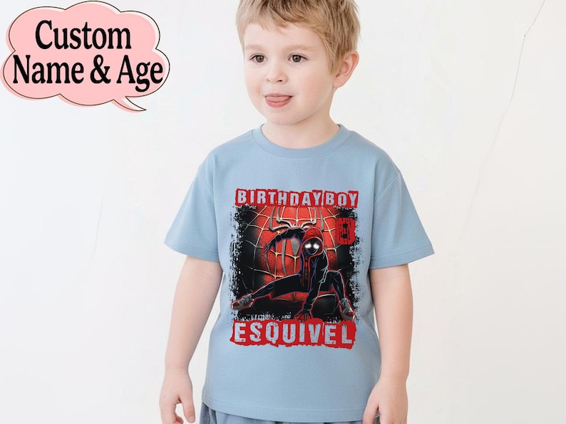 Puede incluir: Camiseta azul claro con un dise&ntilde;o de superh&eacute;roe negro y rojo, con las palabras "BIRTHDAY BOY" y un nombre. La camiseta tiene un dise&ntilde;o desgastado y la lleva un ni&ntilde;o peque&ntilde;o.