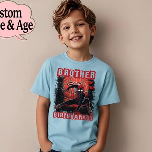 Puede incluir: Camiseta azul claro con un gr&aacute;fico de superh&eacute;roe y el texto "Brother of the Birthday Boy". La camiseta tiene cuello redondo y mangas cortas. Una burbuja de di&aacute;logo rosa muestra "Custom Name & Age".