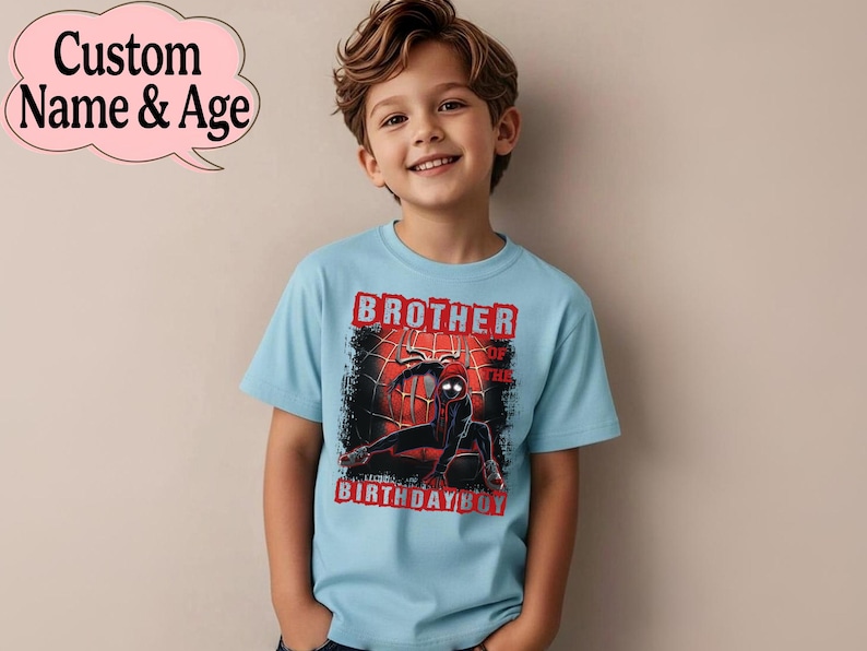 Puede incluir: Camiseta azul claro con un gr&aacute;fico de superh&eacute;roe y el texto "Brother of the Birthday Boy". La camiseta tiene cuello redondo y mangas cortas. Una burbuja de di&aacute;logo rosa muestra "Custom Name & Age".