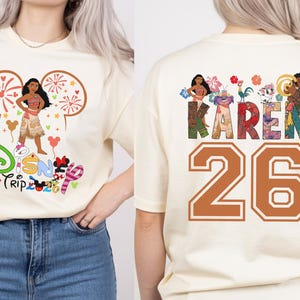 May include: Cream-colored t-shirt featuring a Disney-themed graphic. The front displays a cartoon character with the text "Disney Trip 2020". The back of the shirt has the name "KAREN" and the number "26" in a collegiate style.