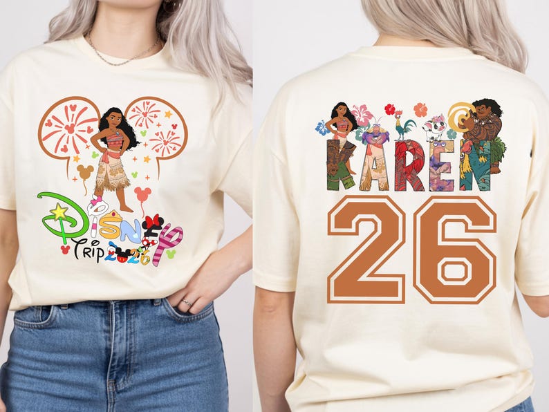 May include: Cream-colored t-shirt featuring a Disney-themed graphic. The front displays a cartoon character with the text "Disney Trip 2020". The back of the shirt has the name "KAREN" and the number "26" in a collegiate style.