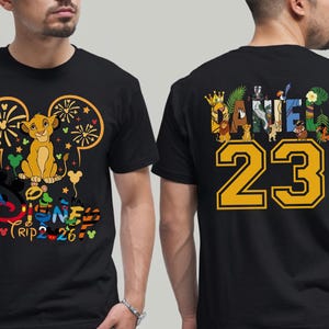 May include: Black t-shirt featuring a Simba graphic with the text "Disney Trip 2-26" on the front. The back of the shirt displays the name "Daniel" with the number "23" in yellow. The design incorporates Disney characters.