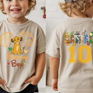 Puede incluir: Camiseta beige de manga corta con un gr&aacute;fico de Simba y el texto "Birthday Boy" en la parte delantera. La parte trasera de la camiseta tiene el nombre "Daniel" y el n&uacute;mero "10" en amarillo.