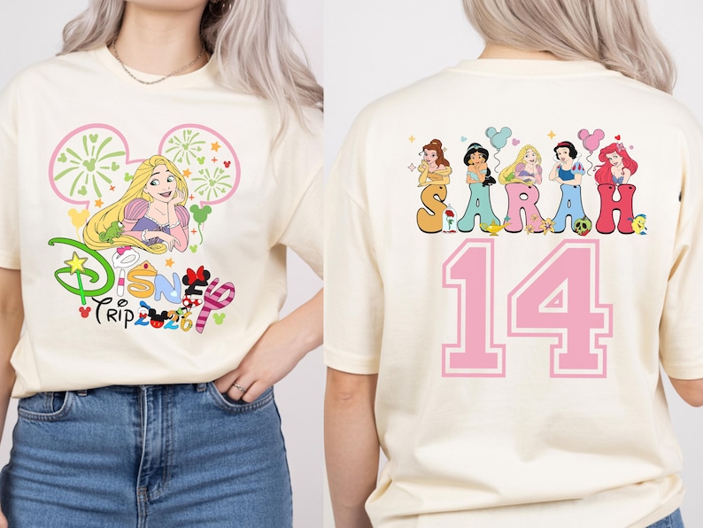 May include: Cream-colored t-shirt featuring a Disney Trip graphic with Rapunzel. The back of the shirt displays the name "SARAH" above the number "14" with Disney princess illustrations.