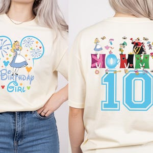 Puede incluir: Camiseta color crema con un dise&ntilde;o de Alicia en el Pa&iacute;s de las Maravillas. La parte delantera muestra a Alicia con un vestido azul, con el texto "Birthday Girl". La parte trasera tiene "Mommy 10" con personajes de Alicia.