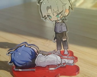 May include: Two anime-style acrylic figures. One figure is standing, with silver hair, a gray jacket, and black pants. The other figure is lying down with blue hair and a white shirt. Both figures are on a red base.