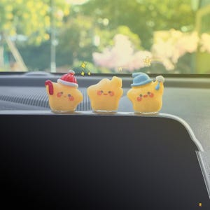 May include: Three yellow star-shaped figurines with smiling faces. The first star wears a red and white Santa hat, the second has no hat, and the third wears a blue hat and holds a small white object. Decorative stars are drawn above the figurines.