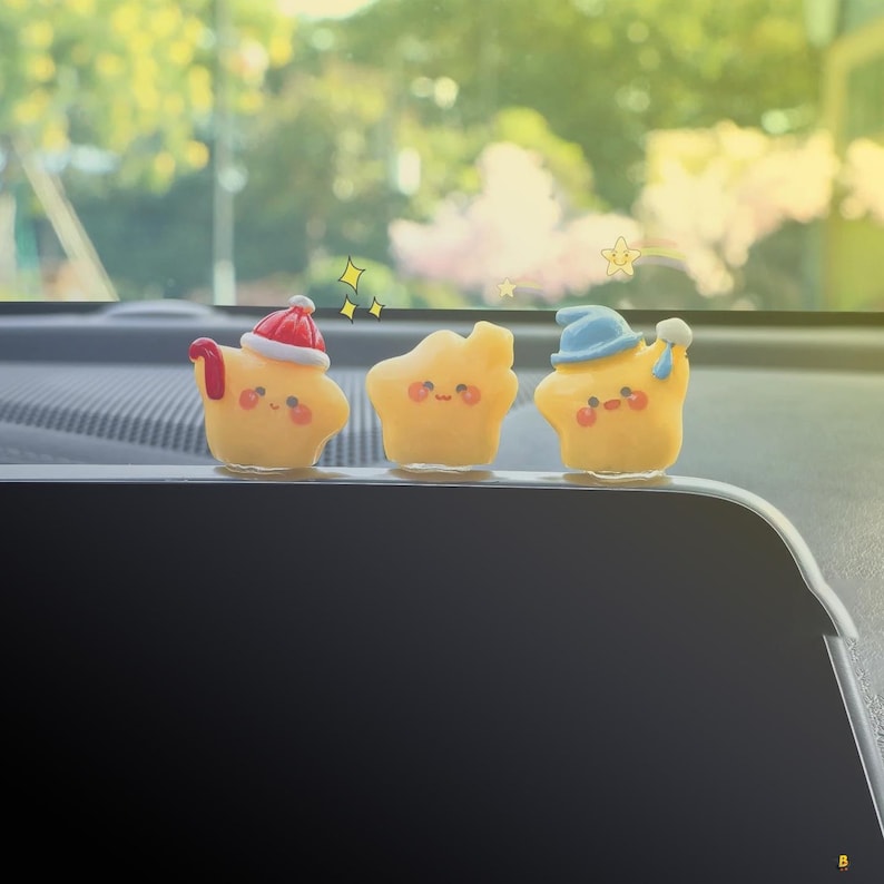 May include: Three yellow star-shaped figurines with smiling faces. The first star wears a red and white Santa hat, the second has no hat, and the third wears a blue hat and holds a small white object. Decorative stars are drawn above the figurines.