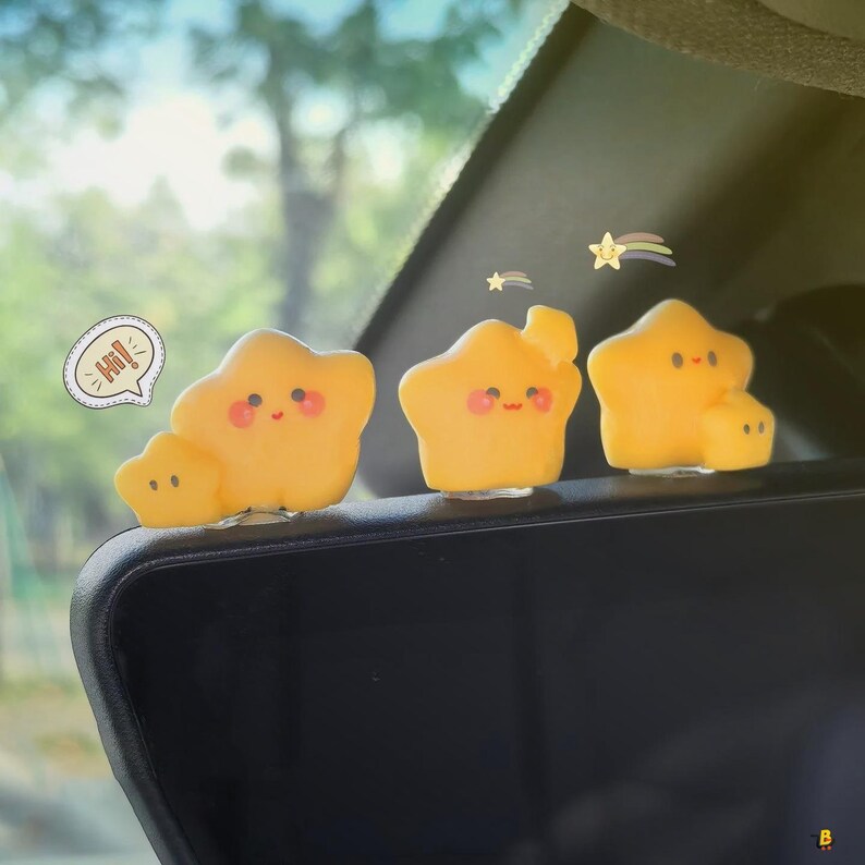 May include: Three yellow star-shaped car accessories with smiling faces and rosy cheeks. One has a small star attached. A speech bubble says "Hi!". A rainbow and star graphic is in the background.