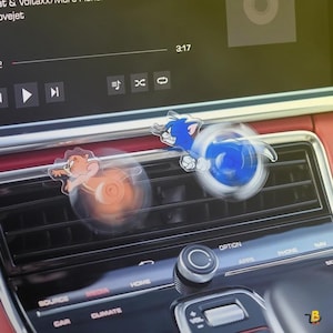 May include: Two car air vent decorations featuring cartoon characters Tom and Jerry. Tom is blue and Jerry is brown. The decorations are spinning, with a blue and orange circular design.
