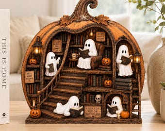 May include: A decorative pumpkin-shaped bookshelf figurine featuring multiple white ghost figures reading books. The scene includes miniature pumpkins, lanterns, a skull, and signs with text like 'A book a day keeps the monsters away' and 'Quiet ghosts reading'.