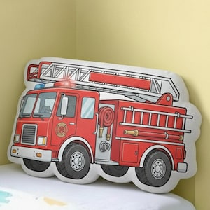 May include: A red and white fire truck shaped pillow with black wheels and a ladder on top. The pillow has a cartoon design and is placed on a white bed.
