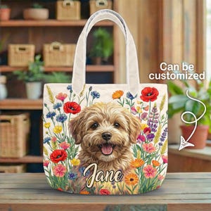 May include: A beige tote bag featuring a smiling dog surrounded by colorful flowers. The dog's name, "Jane," is scripted below. The bag has white handles and the text "Can be customized."