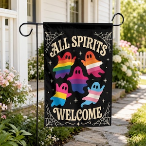 May include: A black rectangular garden flag featuring the text "ALL SPIRITS WELCOME" in a cream-colored font. The design includes five ghosts, each filled with different pride flag colors, surrounded by small star icons and spider web corners.