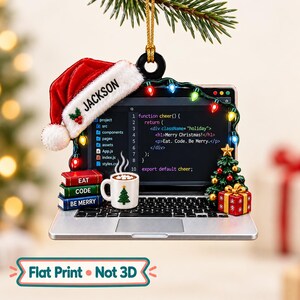 May include: A laptop-shaped Christmas ornament featuring a red Santa hat with the name JACKSON, a screen displaying code, a string of colorful lights, a mug of hot cocoa, a stack of books labeled EAT, CODE, BE MERRY, and a gift box.