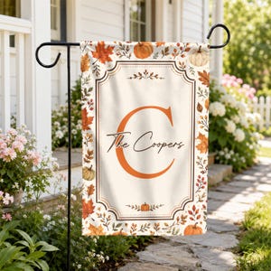 May include: A rectangular garden flag featuring a cream-colored center with a large orange letter C and the text The Coopers in black script. The border is decorated with a pattern of orange, red, and brown autumn leaves, berries, and pumpkins.