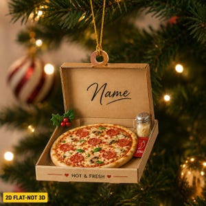 May include: A hanging Christmas tree ornament shaped like a cardboard pizza box containing a miniature pepperoni pizza. The box lid features the text Name and the base reads HOT & FRESH. Includes a tiny shaker and a red chili pepper packet.
