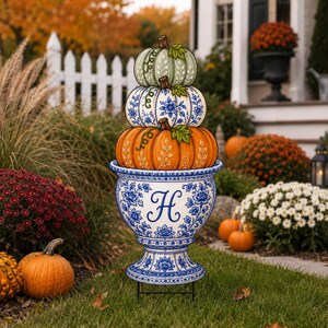 May include: A decorative yard sign featuring a stack of three pumpkins in sage green, blue and white floral, and orange, resting in a blue and white floral urn with a large letter H printed on the front, supported by a black metal stake.