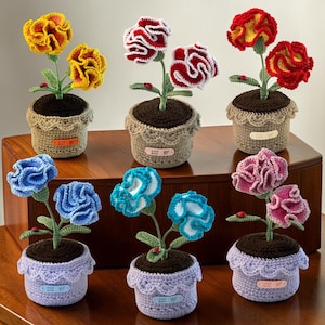 May include: Six crocheted potted flowers in various colours including yellow, red, white, blue, and pink. Each plant features green stems, leaves, and a small ladybug, set in a crocheted pot with a brown top and a small tag labelled Hand Made.