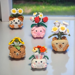 May include: Five handmade crochet animal planters, each with a different flower arrangement. The planters are shaped like a cat, pig, bear, bunny, and bear. The flowers include daisies, strawberries, sunflowers, and other colourful blooms.