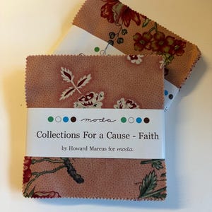 May include: A stack of square fabric swatches featuring a dusty rose background with a floral pattern in red, green, and cream. A white paper band wraps around the centre, printed with the text Collections For a Cause - Faith by Howard Marcus for moda.