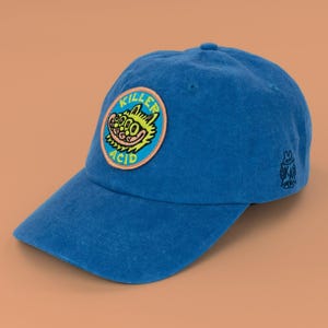 May include: A blue baseball cap featuring a circular patch on the front with a yellow cartoon creature graphic and the text KILLER ACID in blue letters. A small black embroidered logo of a creature with the letters KA is on the side of the cap.