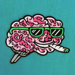 May include: A pink brain with a green and black pair of sunglasses and a white joint coming out of its mouth. The brain is on a white stick.