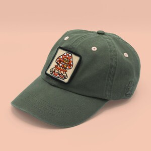 May include: A green baseball cap with a mushroom character patch. The patch is orange, red, and white with a smiling face.