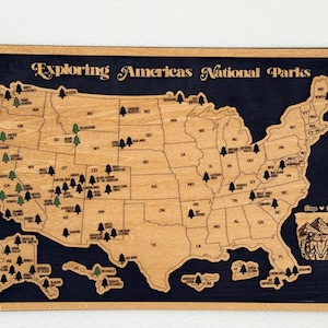 May include: Wooden map of the United States with the text "Exploring Americas National Parks." The map is made of light-colored wood with a dark blue background. Small tree icons mark national park locations.