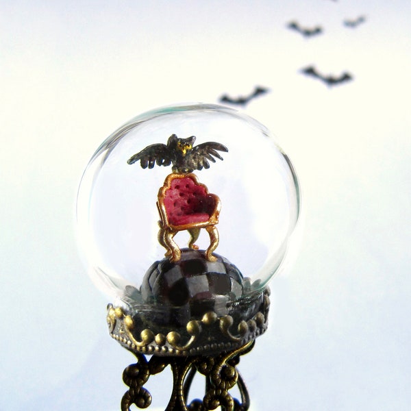 Bague terrarium. Hibou et fauteuil sur sol damier sous une bulle de verre.