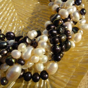 Puede incluir: Un collar hecho de perlas blancas y negras. Las perlas est&aacute;n enhebradas en un cord&oacute;n delgado. El collar est&aacute; sobre una superficie texturizada.