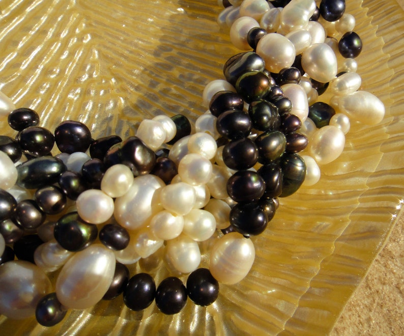 Puede incluir: Un collar hecho de perlas blancas y negras. Las perlas est&aacute;n enhebradas en un cord&oacute;n delgado. El collar est&aacute; sobre una superficie texturizada.