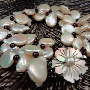 May include: A white pearl and garnet necklace with a large white pearl flower pendant. The necklace is made of multiple strands of pearls and garnets.