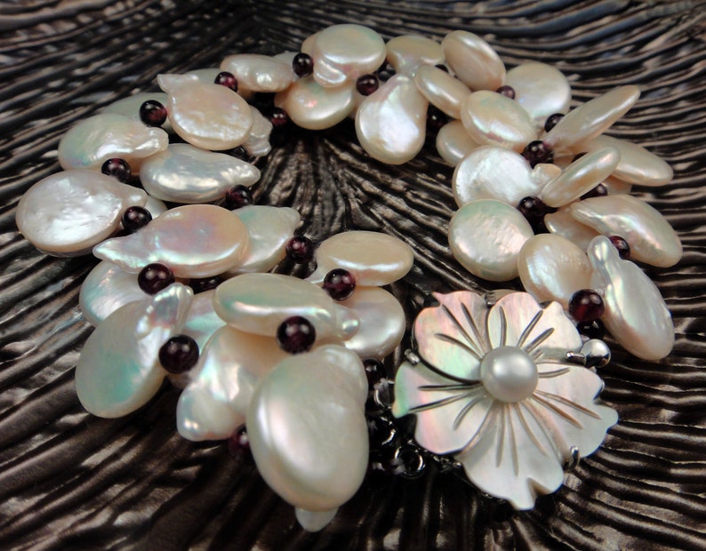 May include: A white pearl and garnet necklace with a large white pearl flower pendant. The necklace is made of multiple strands of pearls and garnets.