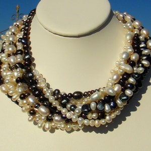 Puede incluir: Un collar de perlas multi-hilo con una mezcla de perlas blancas y negras. El collar est&aacute; hecho de perlas de agua dulce y mide aproximadamente 45 cm de largo.