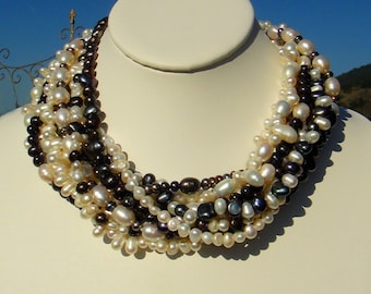 May include: A multi-strand pearl necklace with a mix of white and black pearls. The necklace is made of freshwater pearls and is approximately 18 inches long.