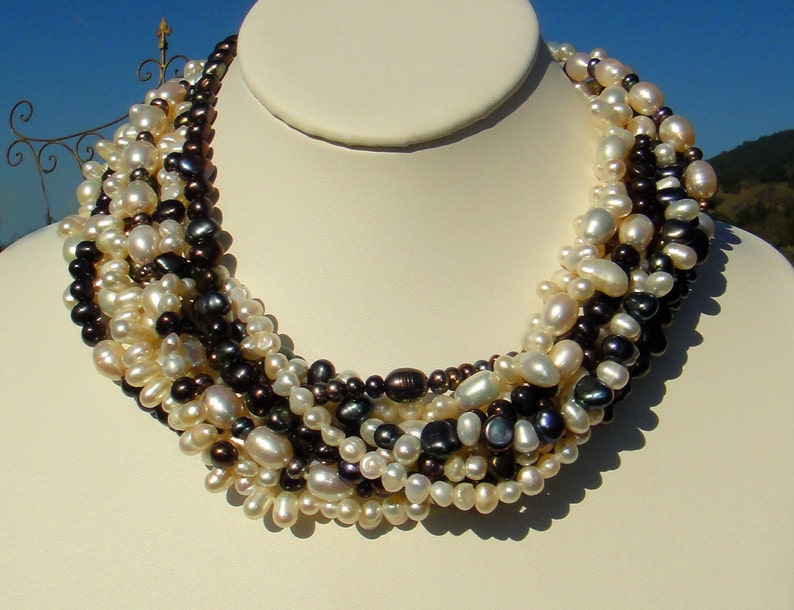 Puede incluir: Un collar de perlas multi-hilo con una mezcla de perlas blancas y negras. El collar est&aacute; hecho de perlas de agua dulce y mide aproximadamente 45 cm de largo.