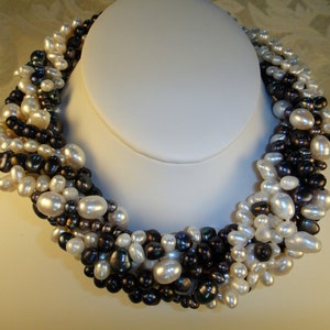 Puede incluir: Un collar de perlas de m&uacute;ltiples hilos con una mezcla de perlas blancas y negras. El collar est&aacute; hecho de una variedad de tama&ntilde;os y formas de perlas, creando un aspecto &uacute;nico y elegante.