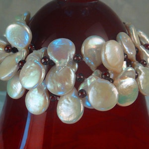 May include: A bracelet made of white baroque pearls and dark red beads. The pearls are arranged in a cluster and the beads are strung between them.