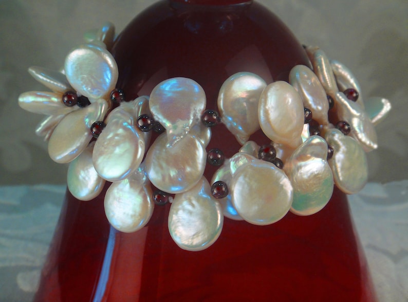 May include: A bracelet made of white baroque pearls and dark red beads. The pearls are arranged in a cluster and the beads are strung between them.
