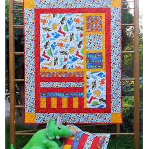 May include: A quilt with a dinosaur theme, featuring a red, yellow, and blue color scheme. The quilt is displayed on a wooden ladder and features a stuffed dinosaur toy in the foreground. The quilt is titled "Forest Frolic" and the fabric is from "Jurassic Jamboree by Ali Hall for Moda".