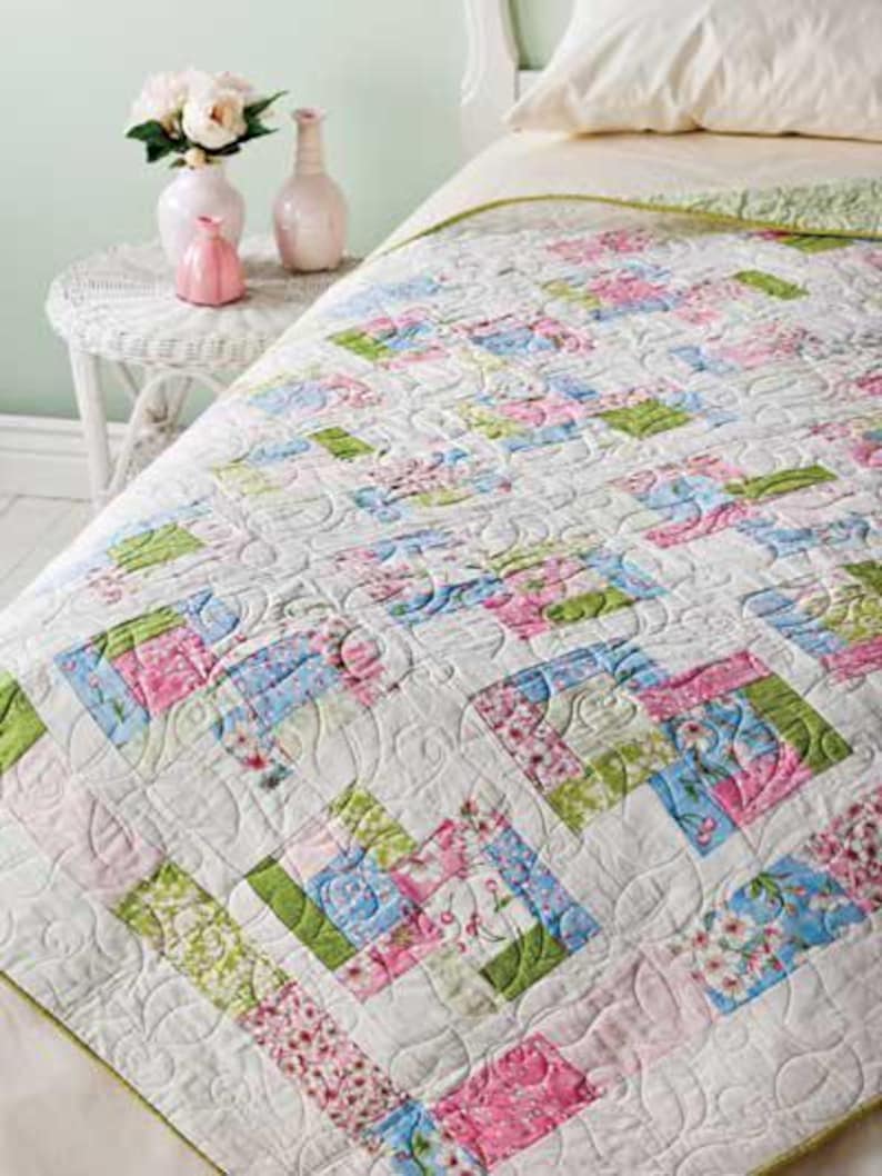 May include: A white quilt with a floral pattern in shades of pink, green, and blue. The quilt is quilted with a swirling pattern.