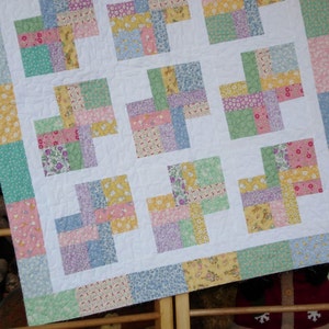 May include: A patchwork quilt with a white background and squares of various pastel colors, including pink, blue, green, and yellow. The quilt is made of different fabrics with floral patterns.