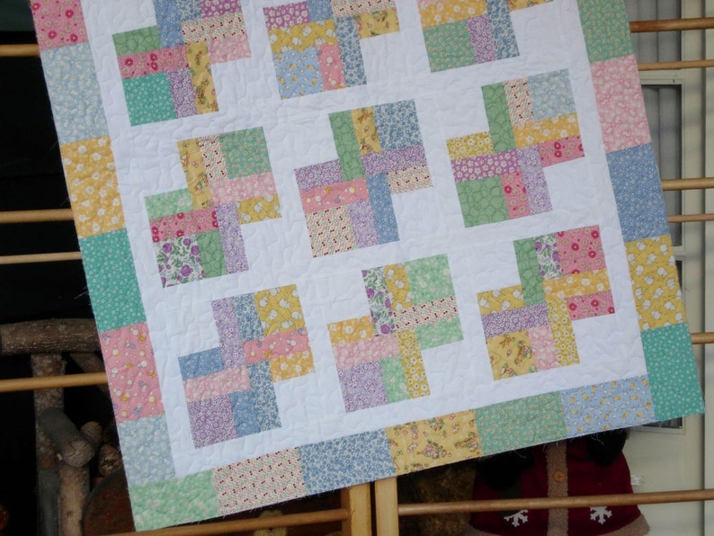 May include: A patchwork quilt with a white background and squares of various pastel colors, including pink, blue, green, and yellow. The quilt is made of different fabrics with floral patterns.