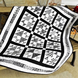 May include: Black and white quilt with a geometric pattern of stars and triangles. The quilt is made with a variety of fabrics and has a black border.