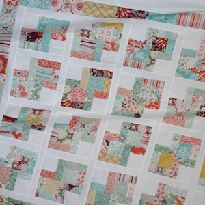 May include: A quilt made of patchwork squares in various shades of blue, green, pink, and yellow. The squares are arranged in a pattern of alternating colors and are sewn together with white fabric.