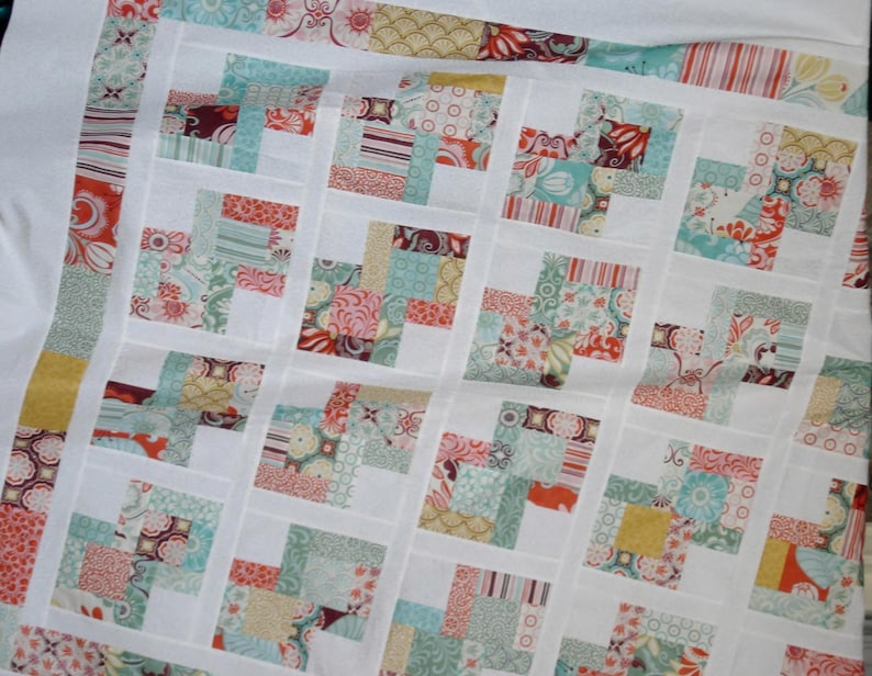 May include: A quilt made of patchwork squares in various shades of blue, green, pink, and yellow. The squares are arranged in a pattern of alternating colors and are sewn together with white fabric.