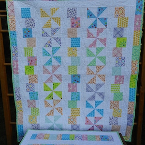 May include: A white quilt with a patchwork design featuring a variety of colorful fabrics. The quilt is made up of squares and triangles, and the fabric patterns include polka dots, flowers, and geometric shapes. The quilt is bordered with a light green trim.
