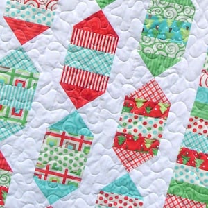 Könnte beinhalten: Eine weiße Steppdecke mit einem sich wiederholenden Muster aus roten, grünen und blauen geometrischen Formen. Die Formen bestehen aus verschiedenen gemusterten Stoffen, darunter Streifen, Punkte und Karos.